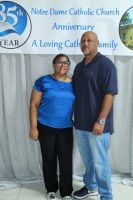 Two people posing in front of a Notre Dame Catholic Church Anniversary backdrop.