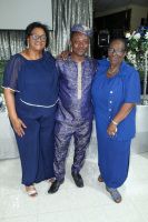 Three people standing indoors, smiling, dressed in blue and purple outfits.