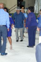 People standing and talking in a hallway, with a man in a blue shirt centered in the scene.