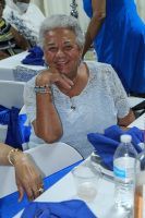 Smiling woman in a white lace top seated at a table with blue tablecloth and water bottle