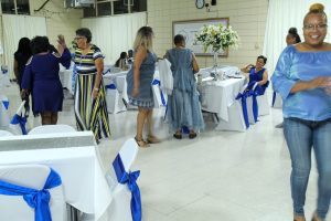People socializing at a decorated indoor event with white tables, blue chair bows, and a buffet table