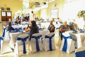 Banquet hall with guests seated at round tables decorated with white cloths and blue bows