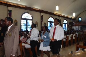 People walking down church aisle during a service, with pews and arched windows visible