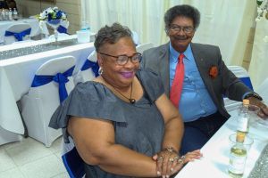Two smiling people seated at a decorated banquet table with blue and white chair bows.