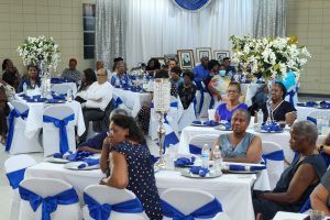 Guests seated at decorated tables in a banquet hall with blue-and-white table settings and floral centerpieces