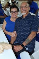Smiling couple seated together at an indoor event, wearing glasses and dark clothing.