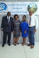 Four people posing indoors in front of a church anniversary banner