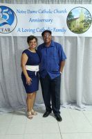 Couple posing together in front of a banner at Notre Dame Catholic Church anniversary celebration