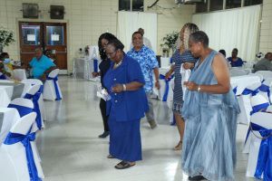 People standing and chatting at a formal indoor event with blue-and-white chair covers