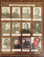 Display of Notre Dame pastors with portrait photos and name labels on a brown wall board