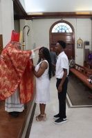 Two people stand before a bishop in a church, one receiving a blessing during a ceremony.