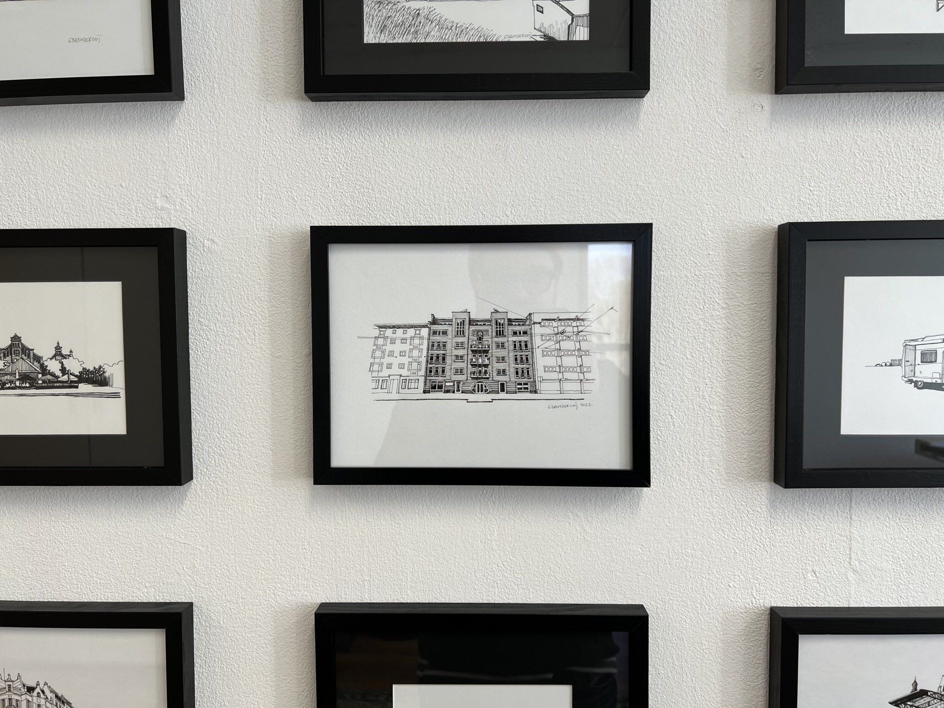 Ingelijste zwart-wit schetsen tentoongesteld op een licht gestructureerde muur.