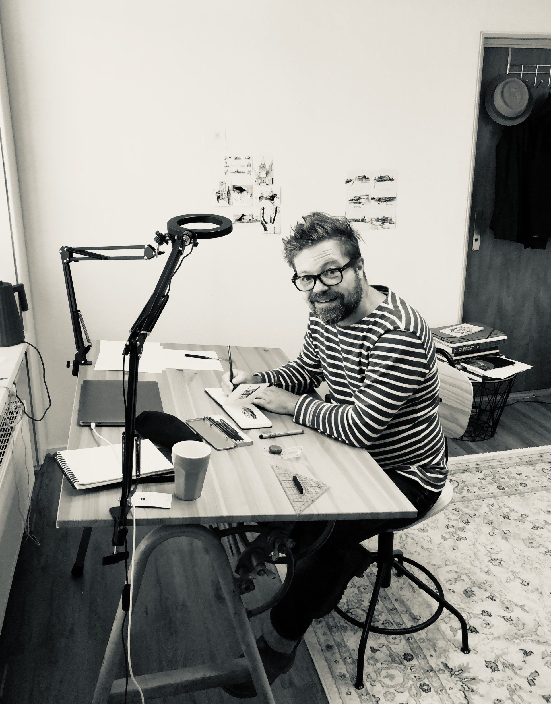 Person smiling at a desk in a home office, writing with papers and a microphone stand nearby.