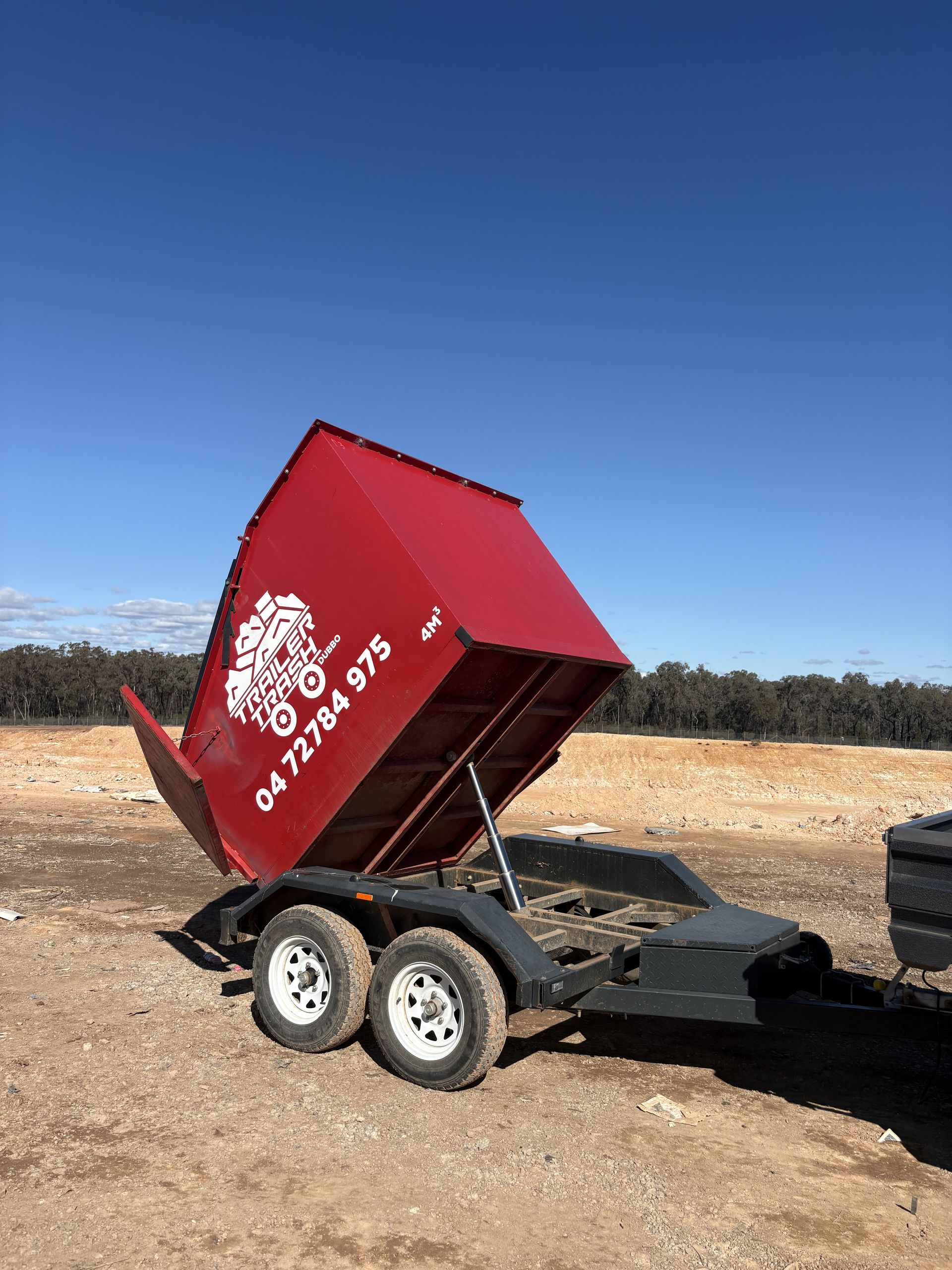 Red Trailer Bed Up, With White Logo and Phone Number on Side, in Dry Field — Trailer Trash Dubbo in Wongarbon, NSW