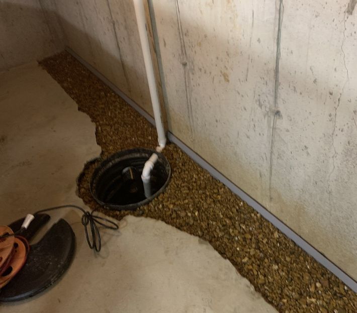 A drain hole in a basement next to a concrete wall