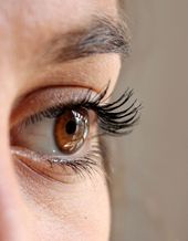 Person getting eyelash extensions applied with tweezers.