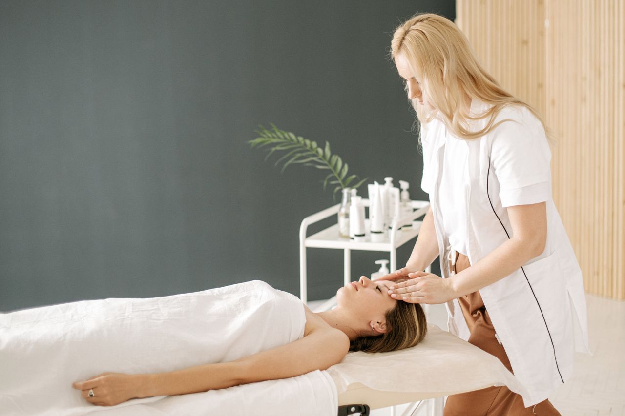 Massage therapist applying head treatment to a client on a spa table in a bright room