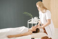 Massage therapist applying head treatment to a client on a spa table in a bright room