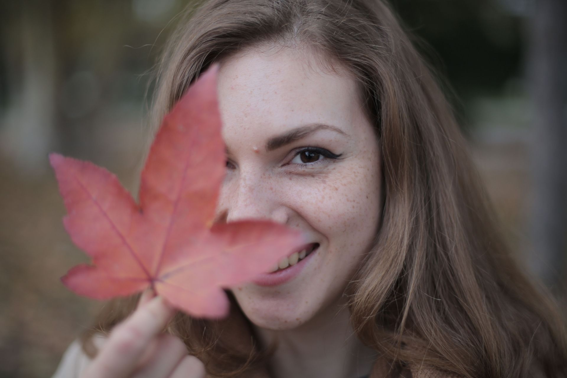Woman smiling behind a red autumn leaf held close to the camera