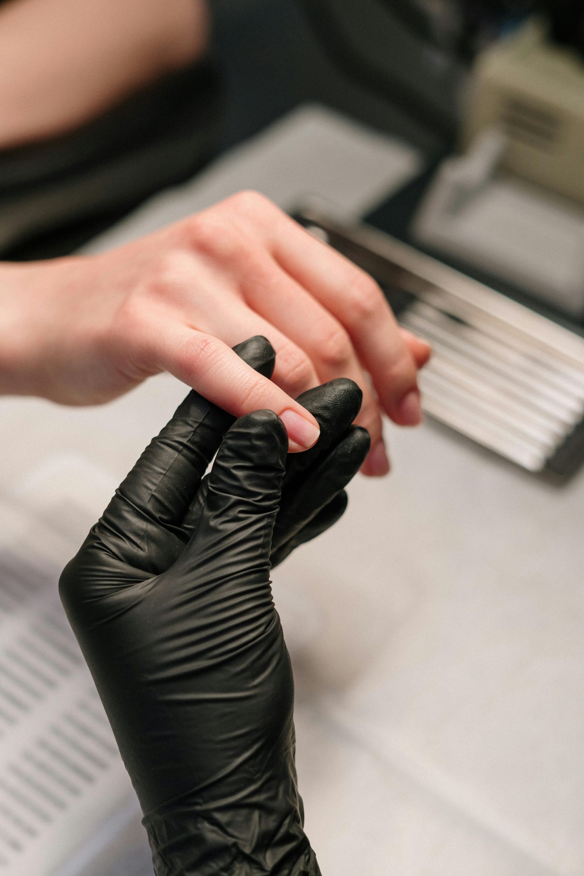 Gloved hand holding another hand, examining a fingernail. Manicurist at work in a salon.
