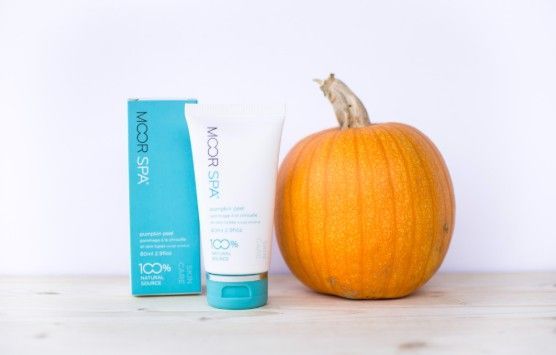 Turquoise tube and white bottle beside a small orange pumpkin on a white surface