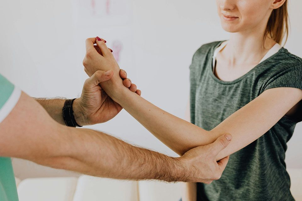 Doctor examining a patient's arm, checking elbow flexibility in a white room.