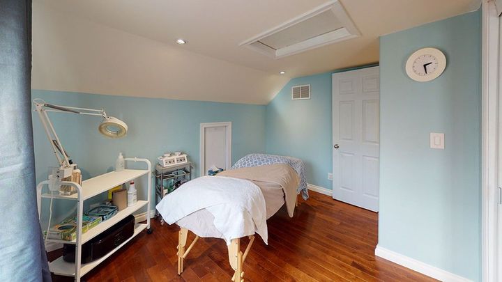 Spa room with treatment bed, equipment, and shelves against blue walls and wood floor.