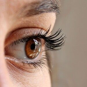 Person getting eyelash extensions applied with tweezers.