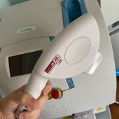 Hand holding a white laser hair removal device in front of a larger machine with a digital display.