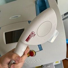 Hand holding a white laser hair removal device in front of a larger machine with a blue and white case.