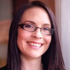 Woman with dark hair and glasses smiles at the camera.