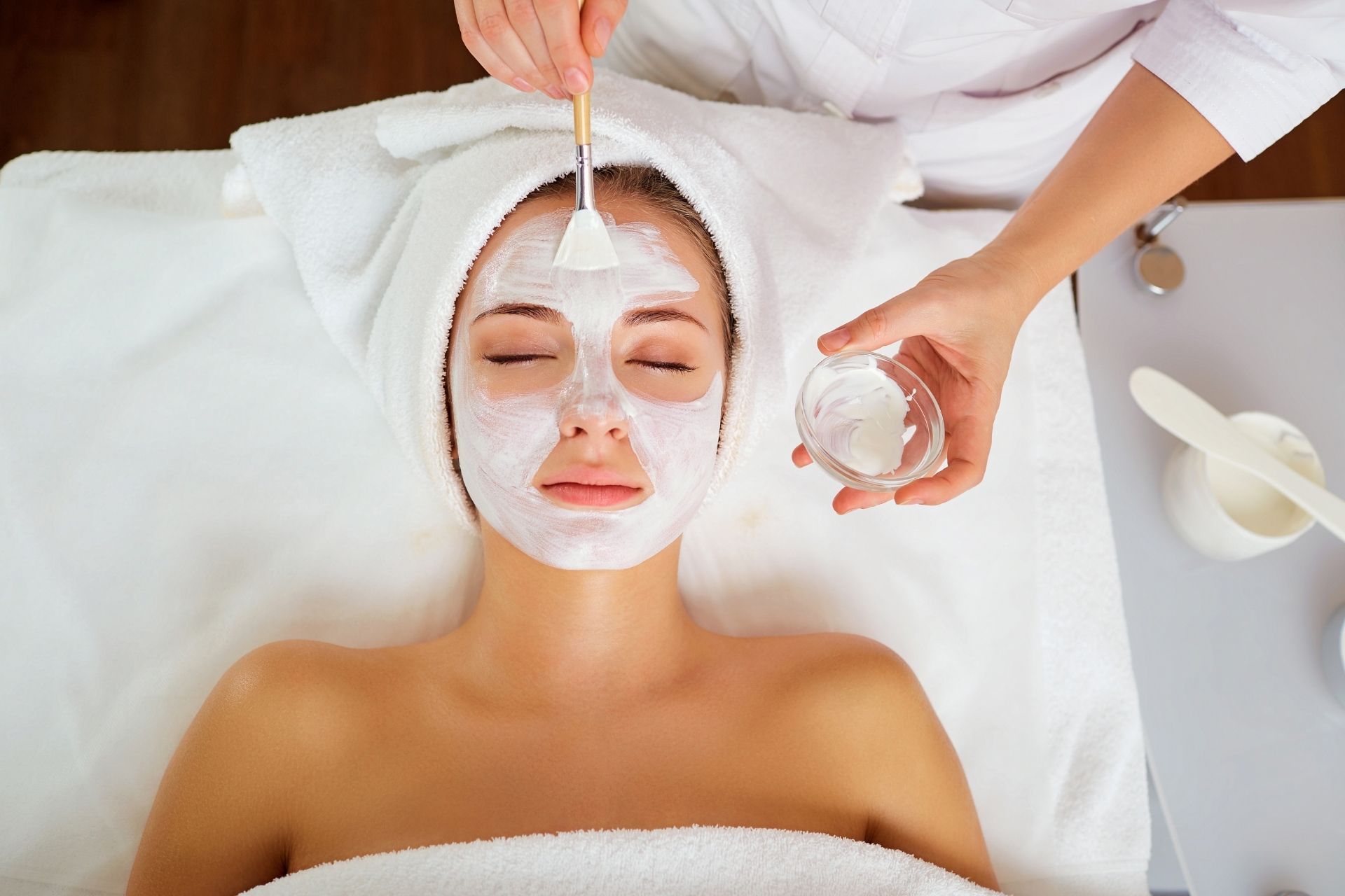 Facial treatment in progress, with a person lying on a spa bed while white cream is applied to their face.