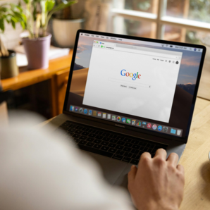 Person using a laptop with Google search open, coffee cup on table, near a window.