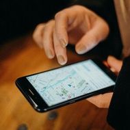 Person using smartphone, navigating map app on a wooden table.