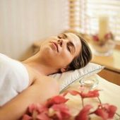 Woman relaxing on a massage table, eyes closed, spa setting.