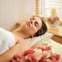 Woman relaxed on a massage table, eyes closed, with flowers in the foreground; spa setting.