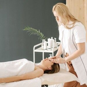Massage therapist applying head treatment to a client on a spa table in a bright room