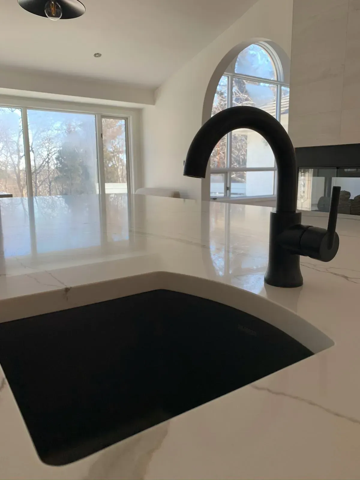 A kitchen sink with a black faucet on a white counter top.