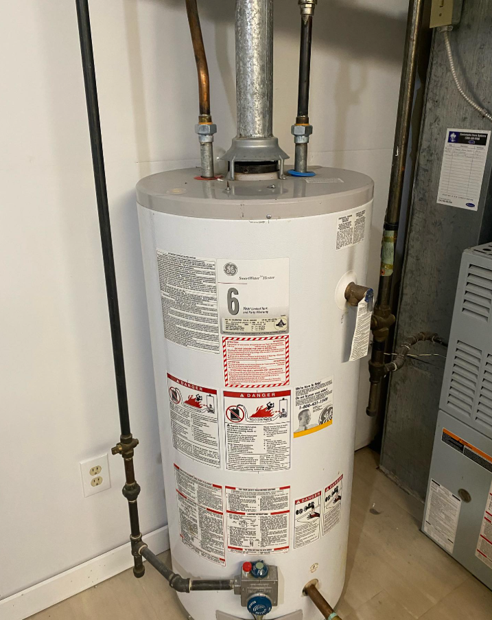 A GE water heater with copper pipes and a flue in a utility space with a furnace.