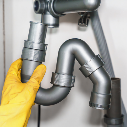 Person in workwear servicing a water heater. She’s kneeling, using a wrench. A toolbox sits open in front.