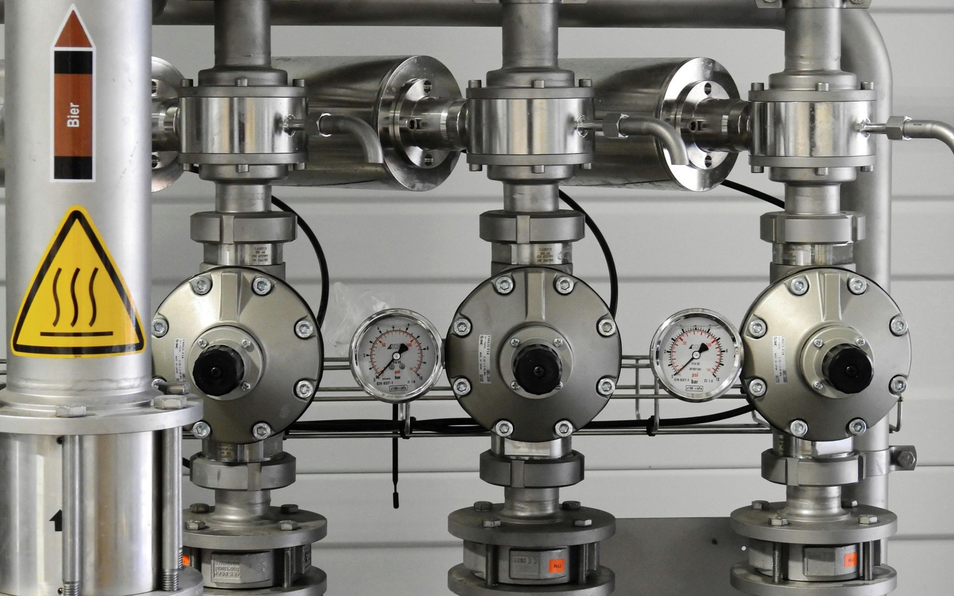 Industrial piping with valves, gauges, and warning signs.