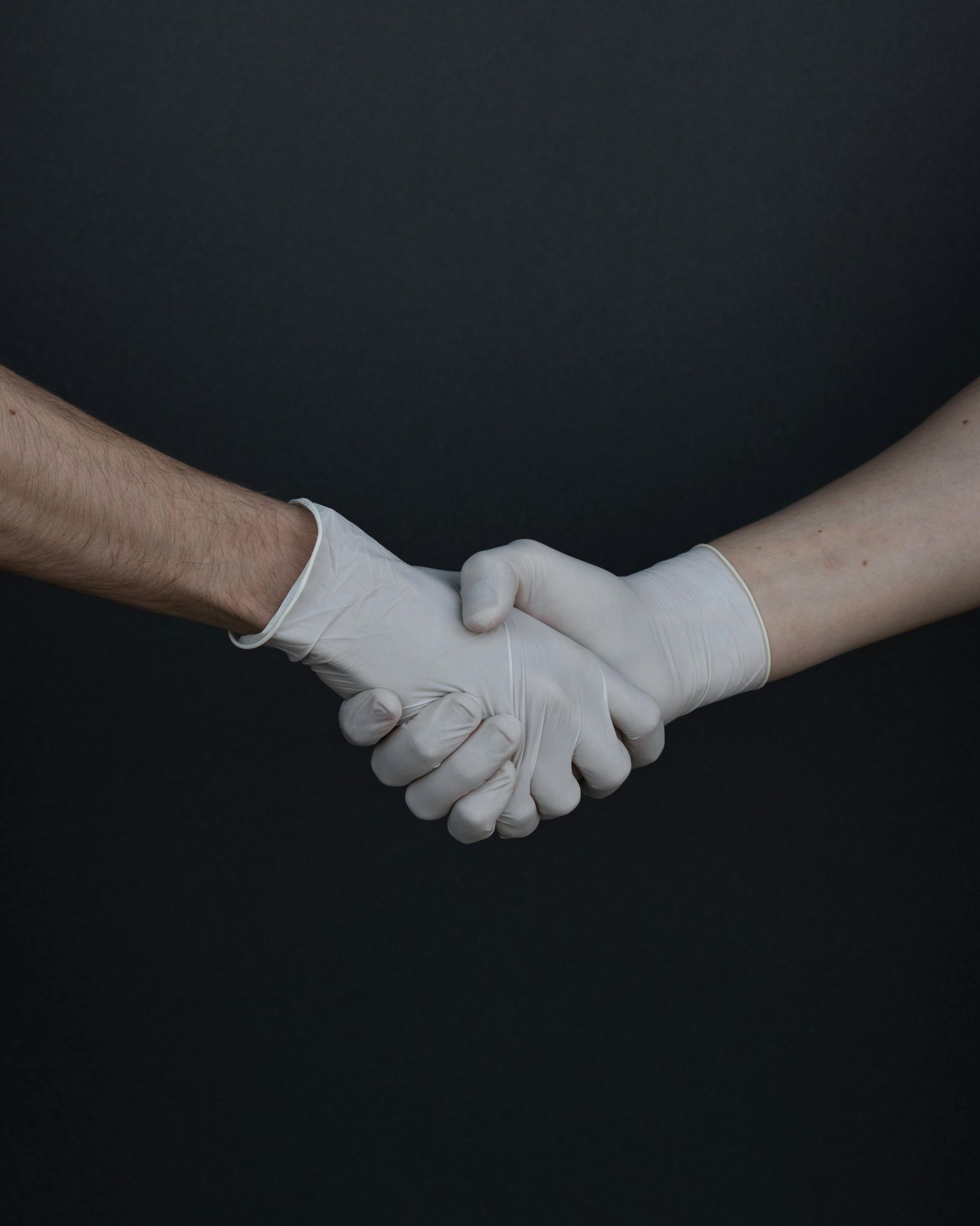 Two gloved hands shaking against a dark background.