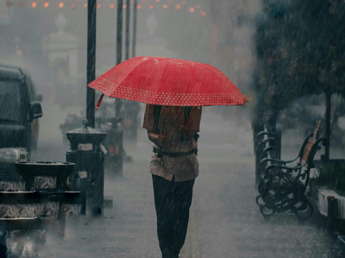 Person under a red umbrella walking in heavy rain on a city street
