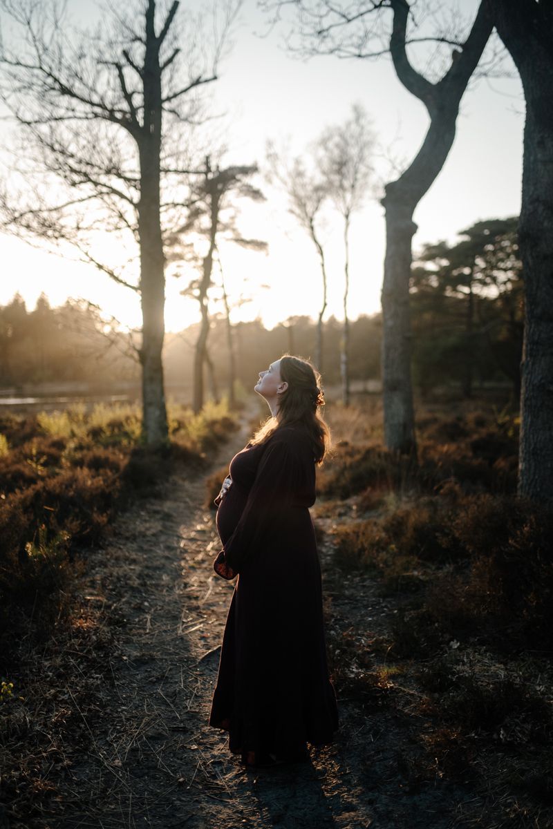 Vrouw in een lange paarse jurk kijkt naar een mooie zonsondergang in het bos