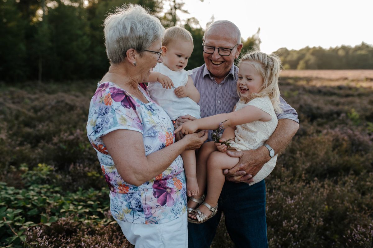 Twee oudere volwassenen houden een lachend kind vast in een grasveld bij zonsondergang.