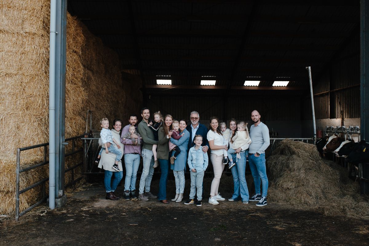 Een groep mensen staat samen in de deuropening van een schuur, met hooibalen op de achtergrond.