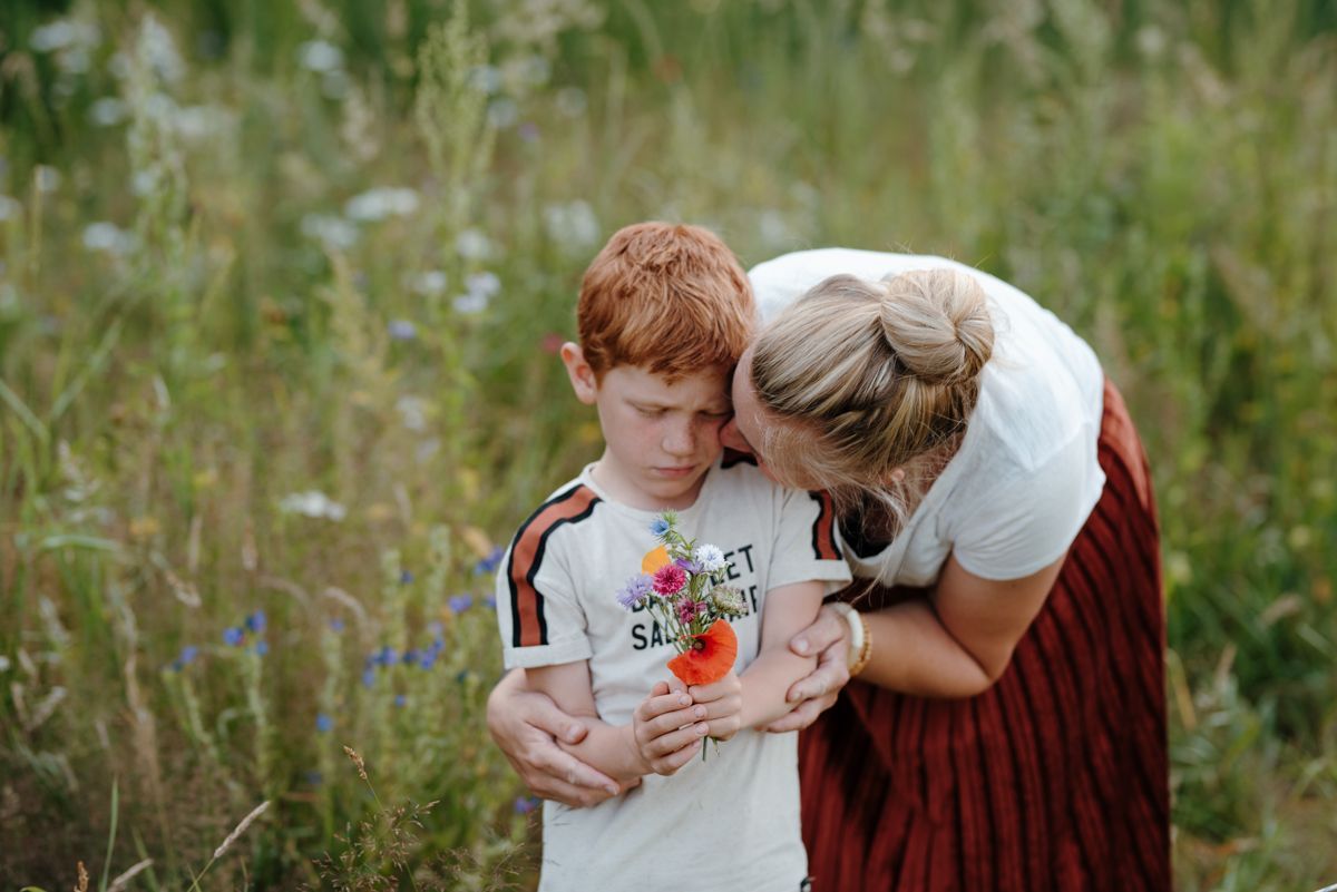 Een vrouw kust een jongen op de wang in een veld.