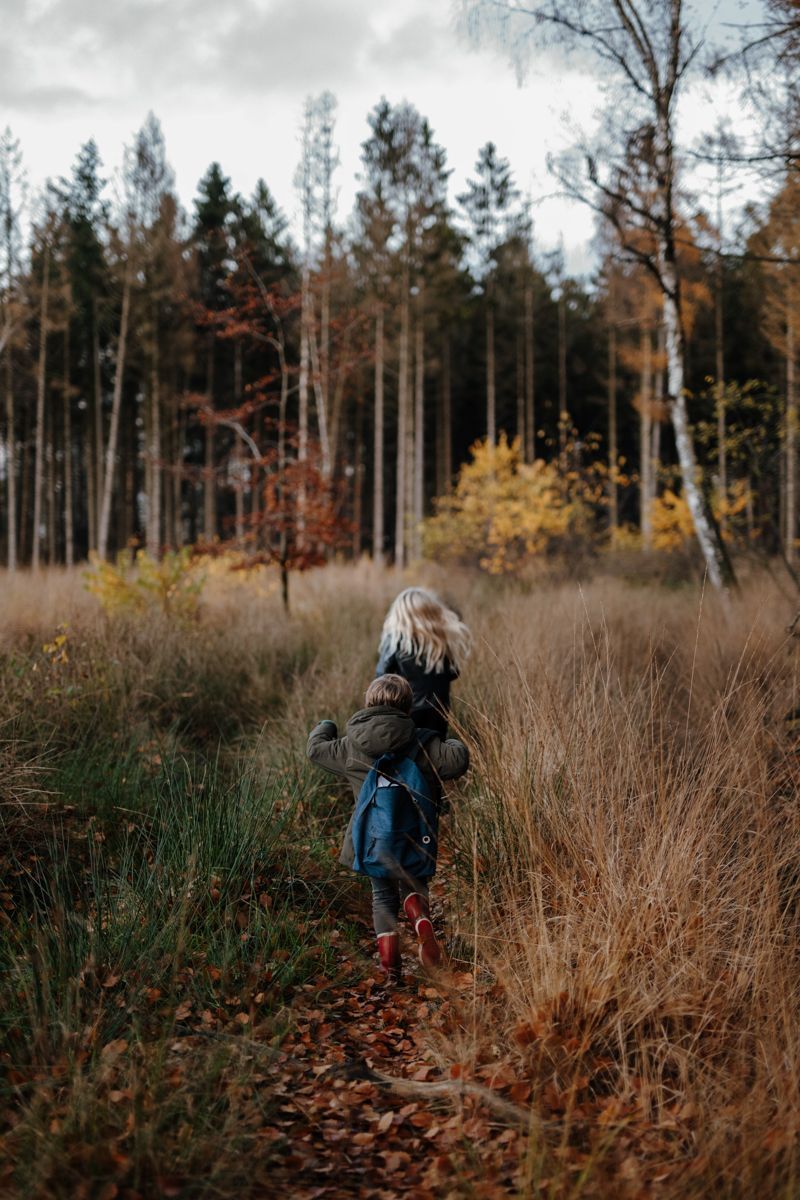 Twee kinderen rennen door het bos met een rugzak vol herfstbladeren