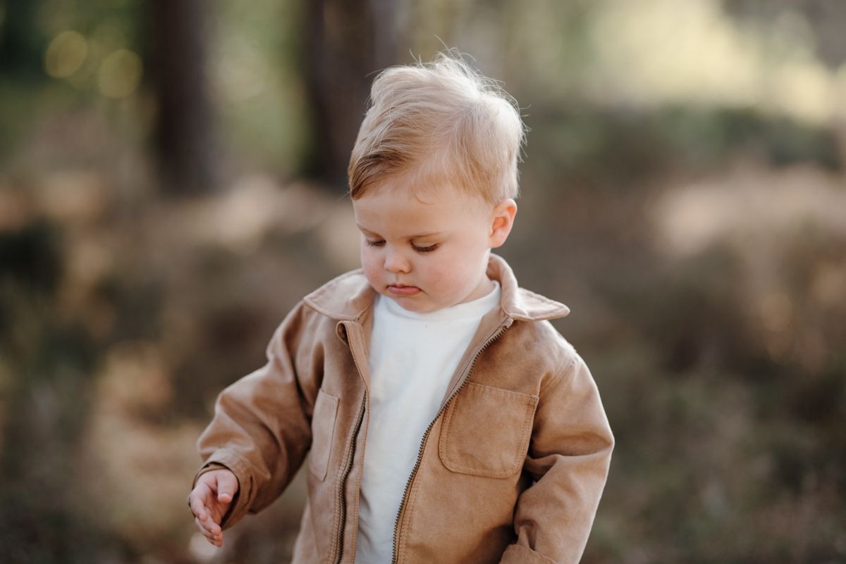 Jong kind in een beige jasje kijkt naar beneden, naar buiten, met een zacht wazige achtergrond.
