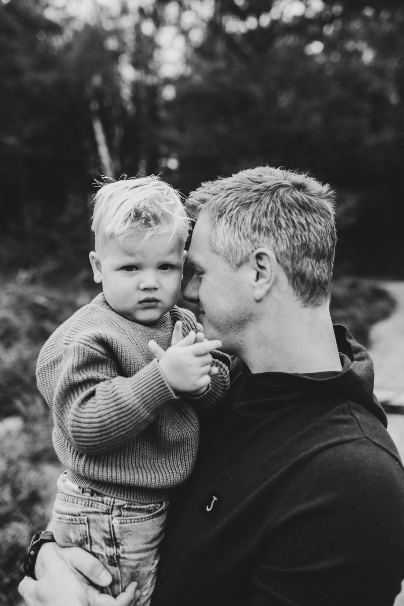 Een volwassene houdt een jong kind buiten vast, beiden gekleed in warme truien, waarbij het kind het gezicht van de volwassene aanraakt.